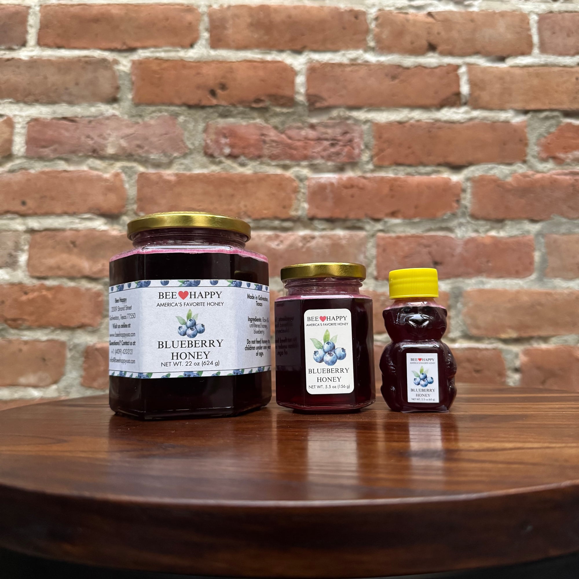22 oz jar, 5.5 oz jar and 2.3 oz bear bottle of Blueberry Honey on a wooden surface with a brick wall background