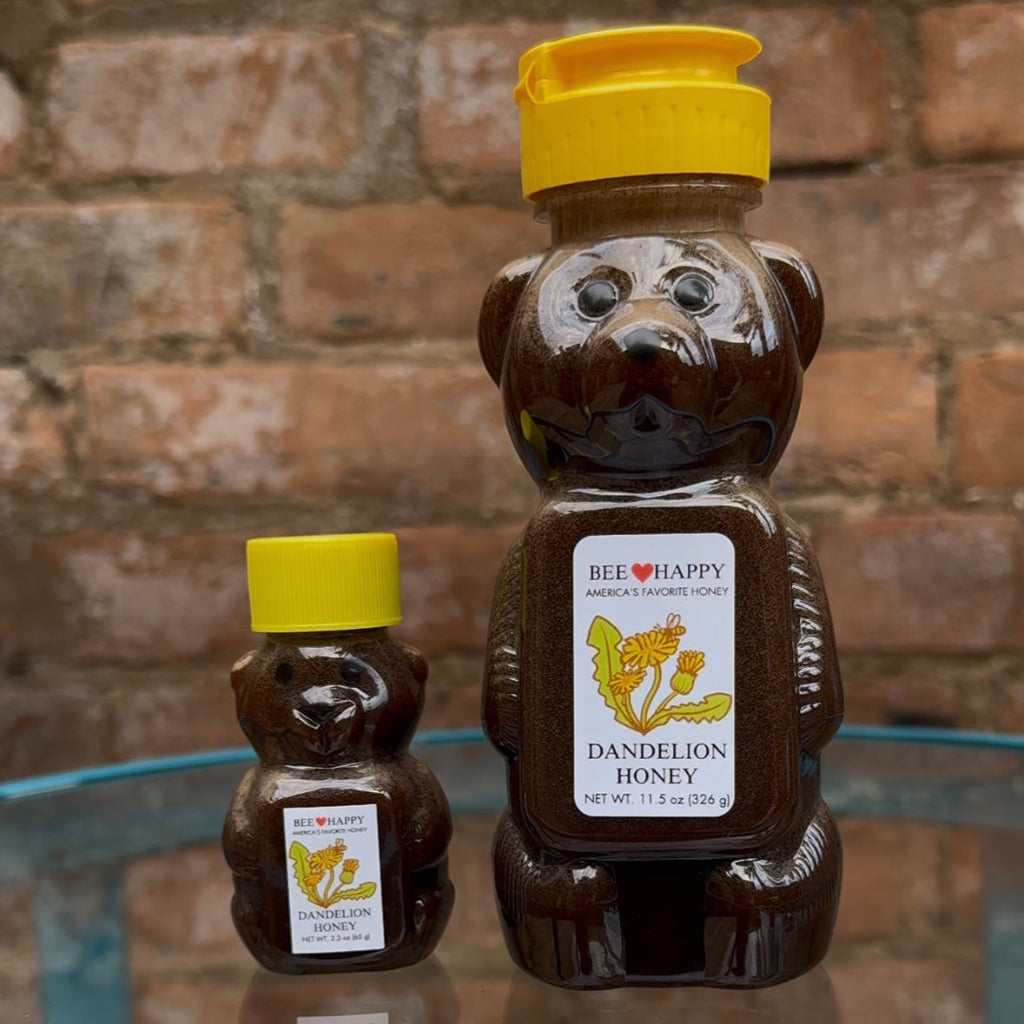 2.3 oz and 11.5 oz Dandelion Honey bear bottles from Bee Happy on a glass surface against a brick wall.