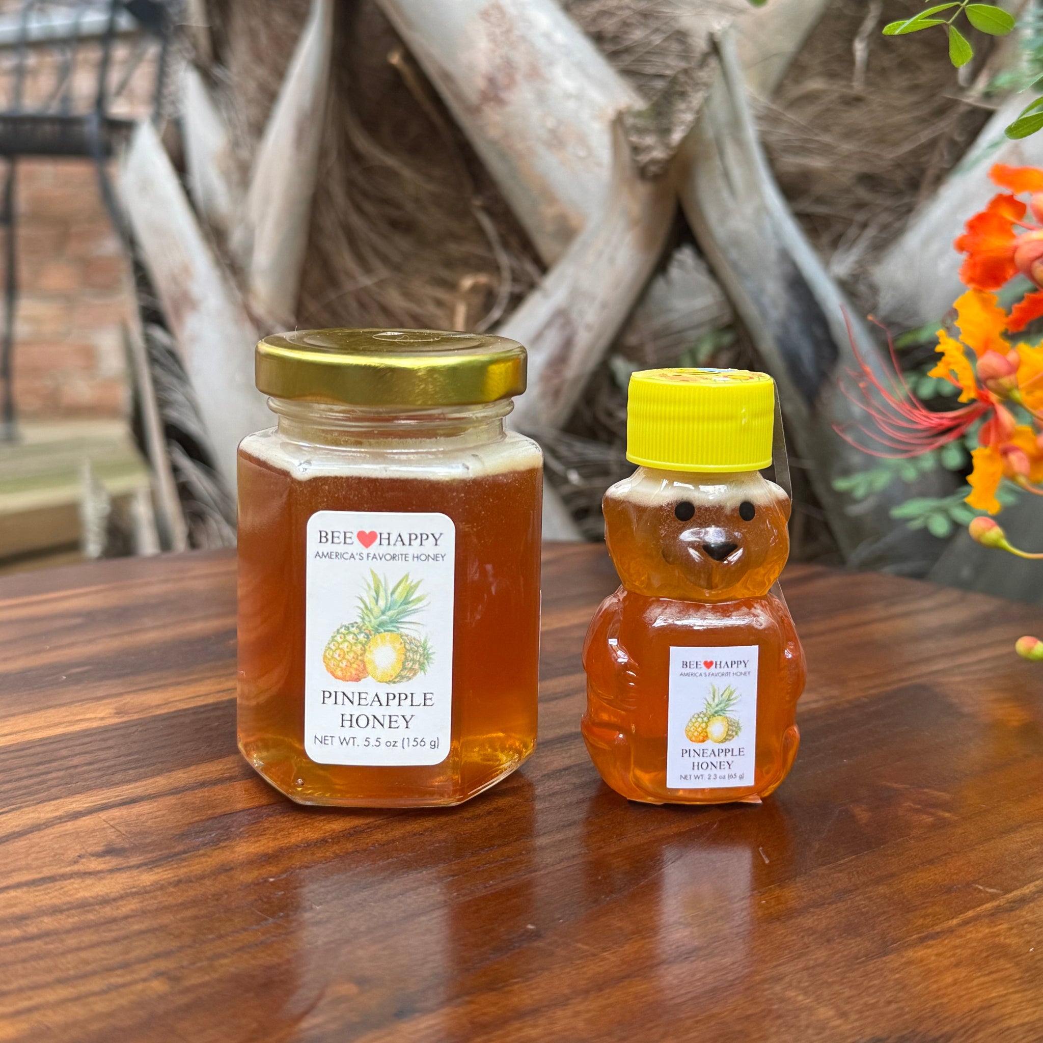 5.5 oz jar and 2.3 oz bear bottle of Pineapple Honey on wooden surface with tree in the background