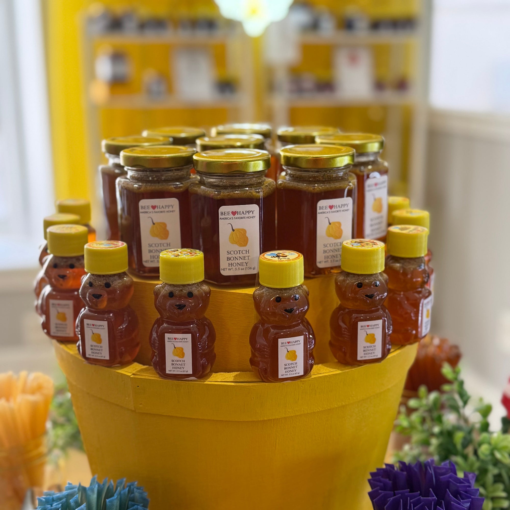 5.5 oz jars and 2.3 oz bears bottles  of Scotch Bonnet Honey on wooden display with blurred background