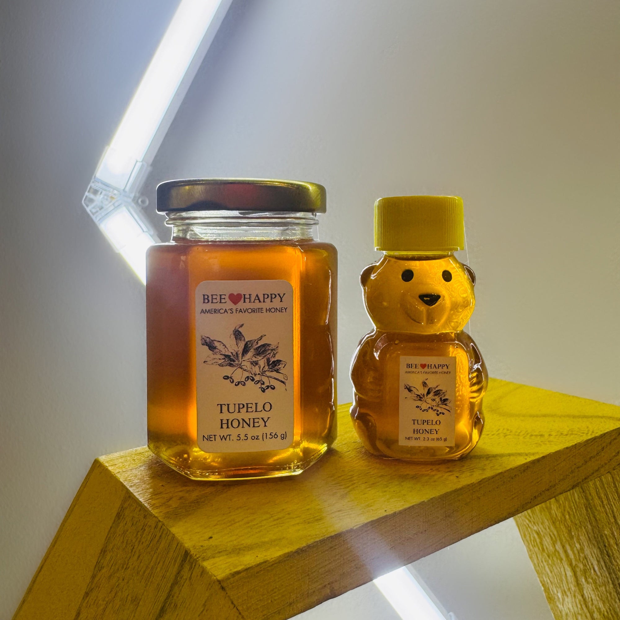 5.5 oz Jar and 2.3 oz bear-shaped bottle of Tupelo Honey on a wooden surface with a neutral background