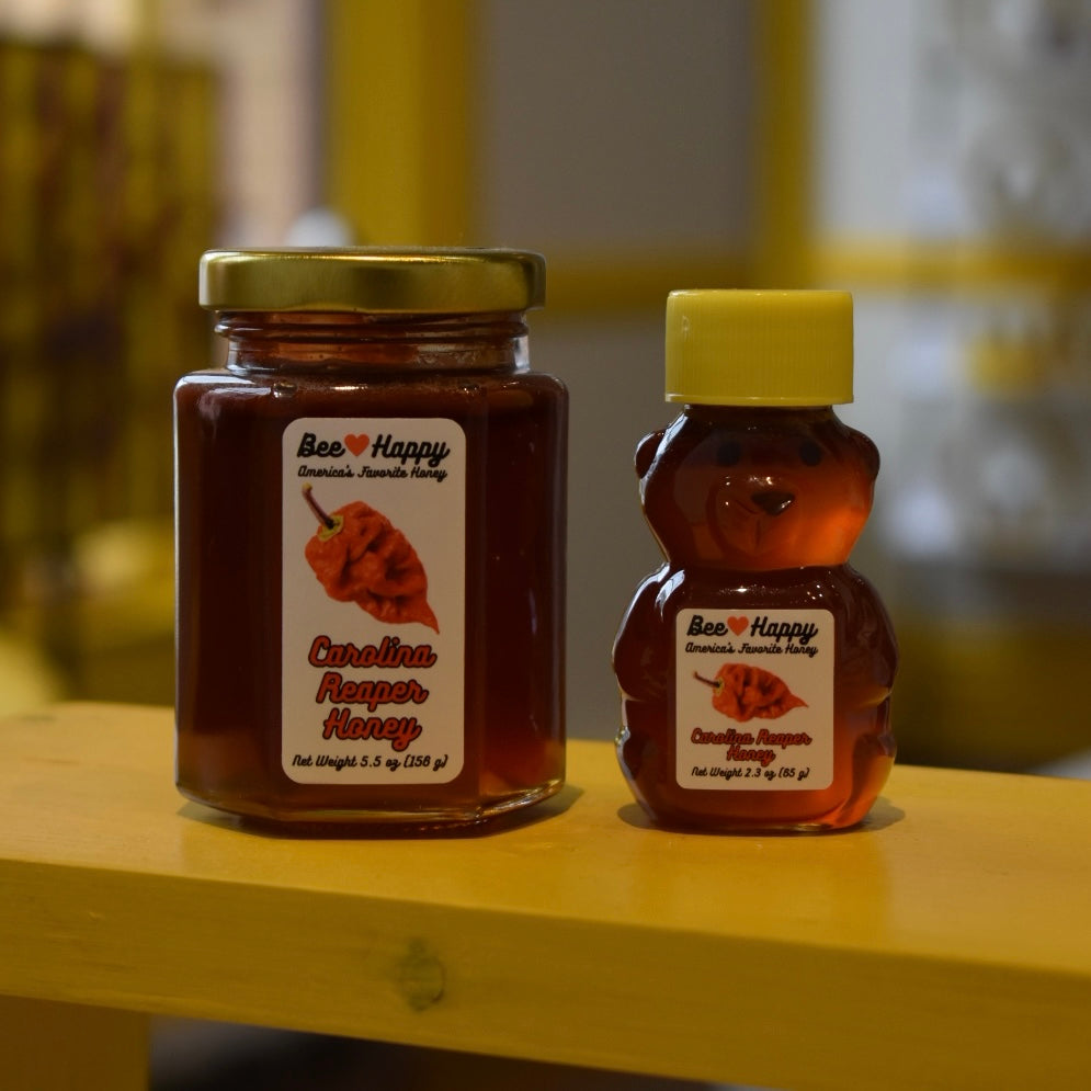 5.5 oz jar and 2.3 oz bear bottle of Carolina Reaper Honey on a wooden surface with a blurred background.