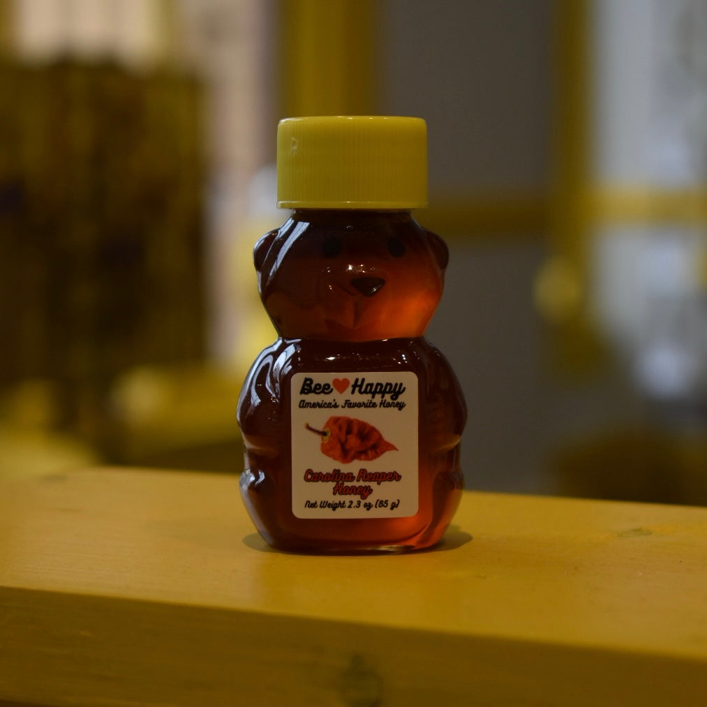 2.3 oz bear bottle of Carolina Reaper Honey on a wooden surface with a blurred background.