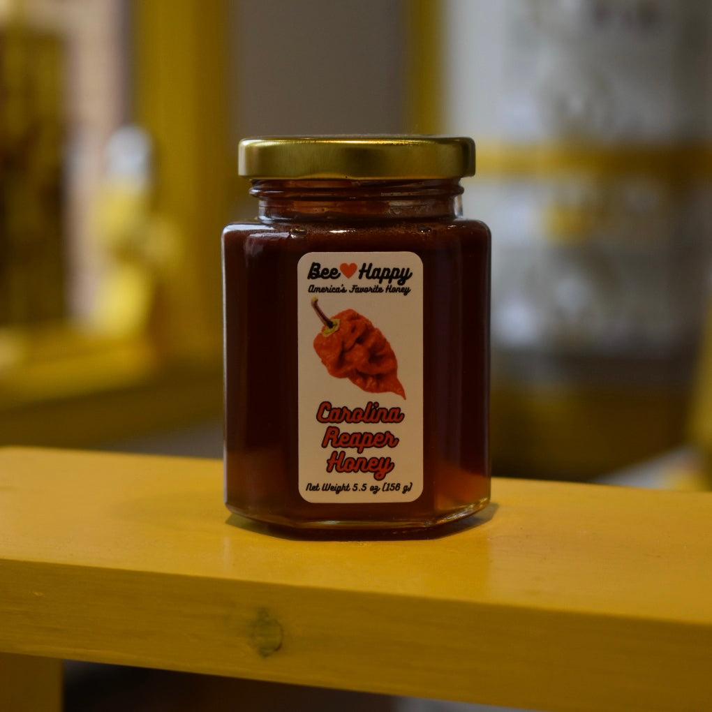 5.5 oz jar of Carolina Reaper Honey on a wooden surface with a blurred background.