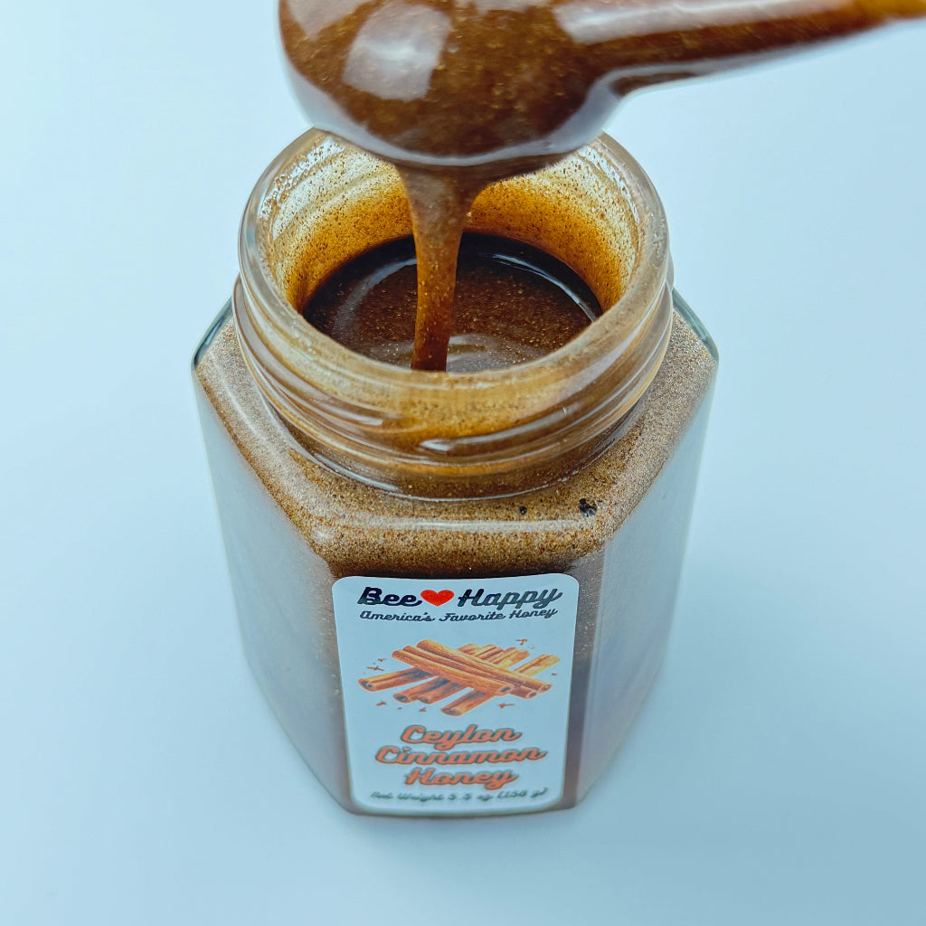 A honey dipper dipped in a 5.5 oz jar of Ceylon Cinnamon Honey on a white background