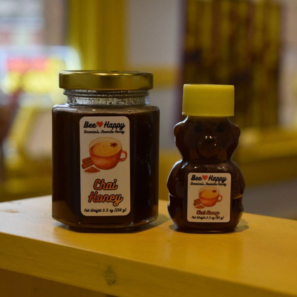 5.5 oz jar and 2.3 oz bear bottle of Chai Honey on a wooden surface with a blurred background.