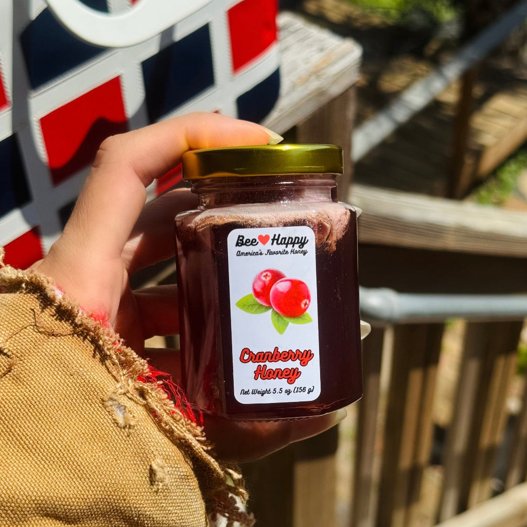 Hand holding a 5.5 oz jar of Cranberry Honey against a blurred background.