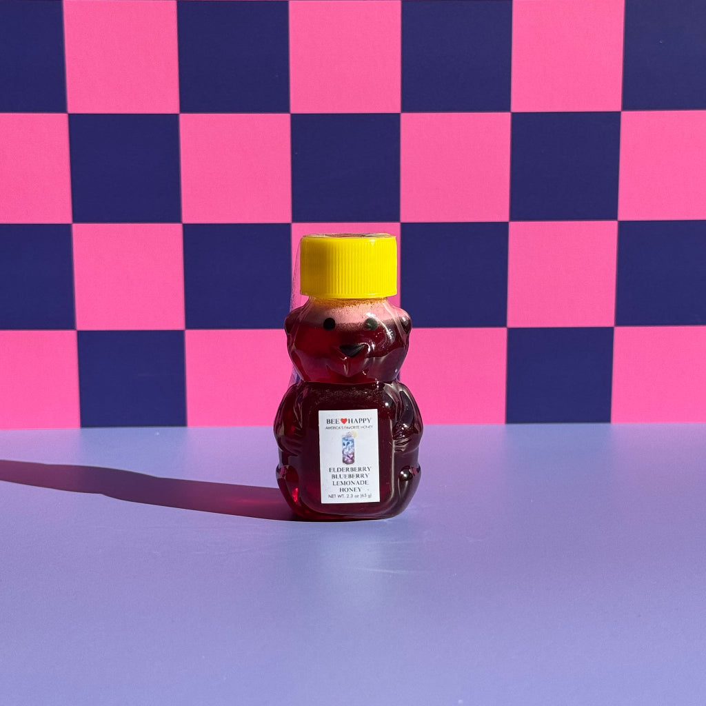 2.3 oz bear bottle of Bee Happy Elderberry Blueberry Lemonade on a pink and blue checkered background