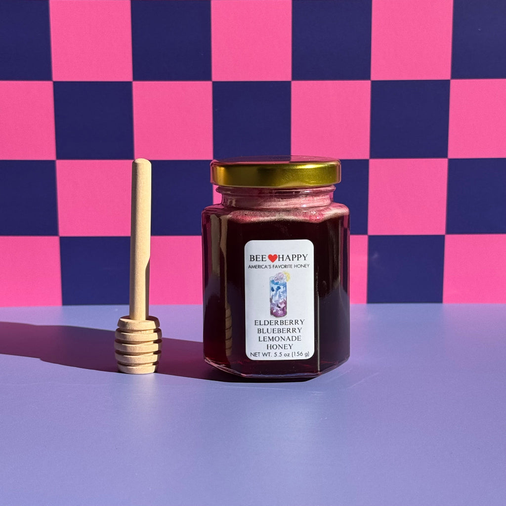 5.5 oz jar of Bee Happy Elderberry Blueberry Lemonade and a honey dipper on a pink and blue checkered background