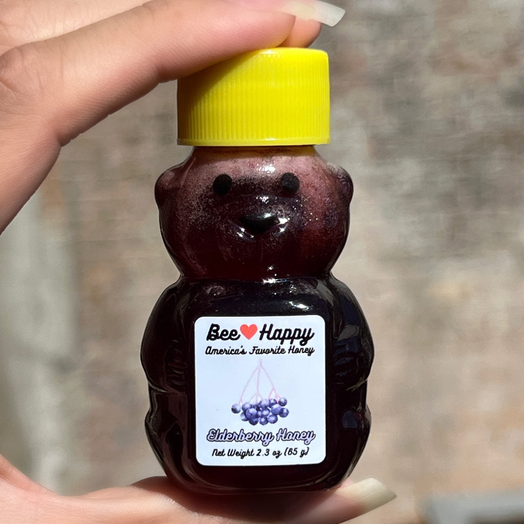 2.3 oz bear bottle of Elderberry Honey with yellow lid held by a hand against a blurred background