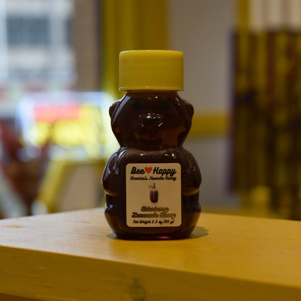 2.3 oz bear bottle of Elderberry Lemonade Honey on a wooden surface with a blurred background.