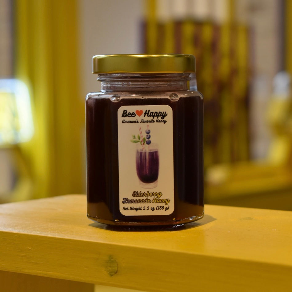 5.5 oz jar of Elderberry Lemonade Honey on a wooden surface with a blurred background.