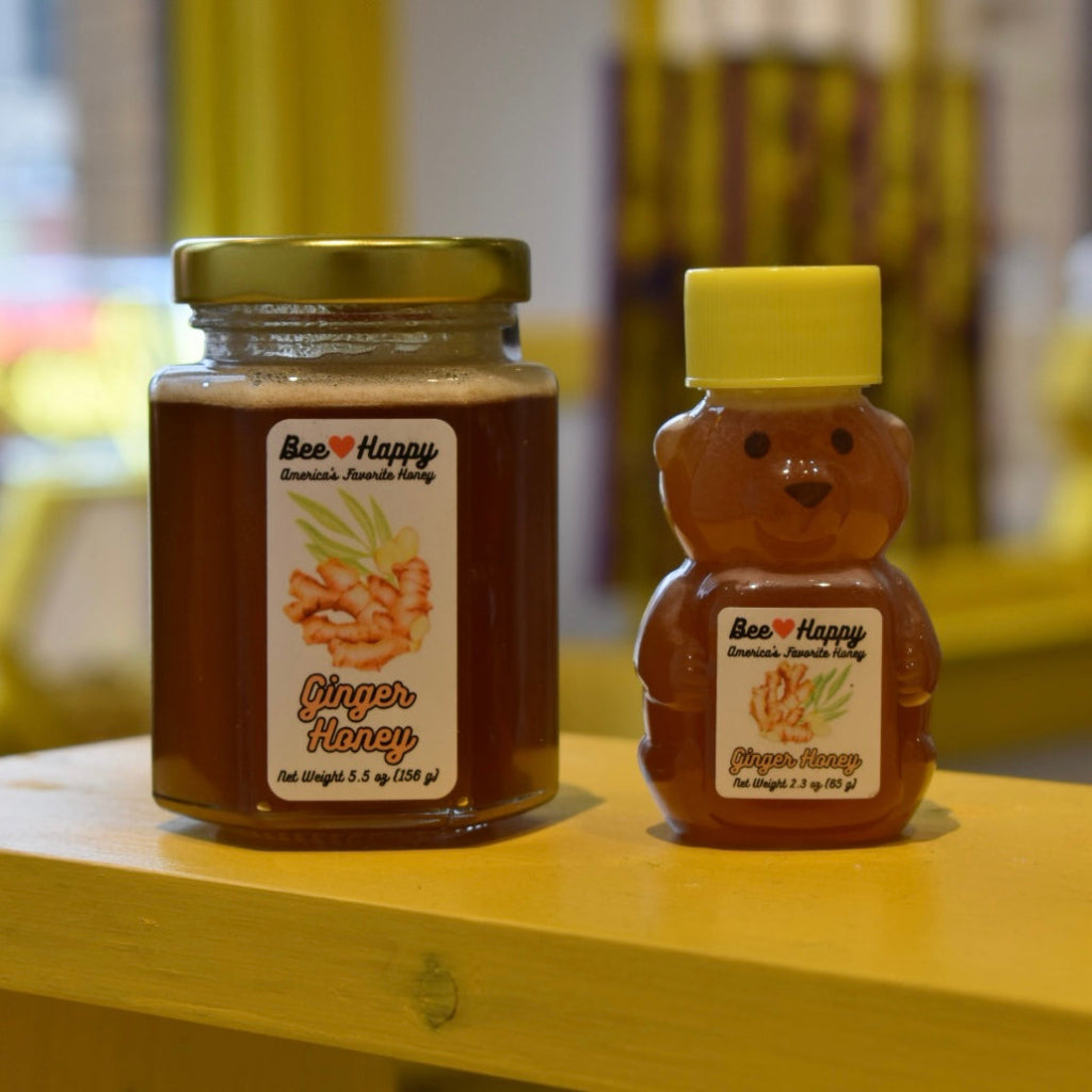 5.5 oz jar and 2.3 oz bear bottle of Ginger Honey on a wooden surface with a blurred background.