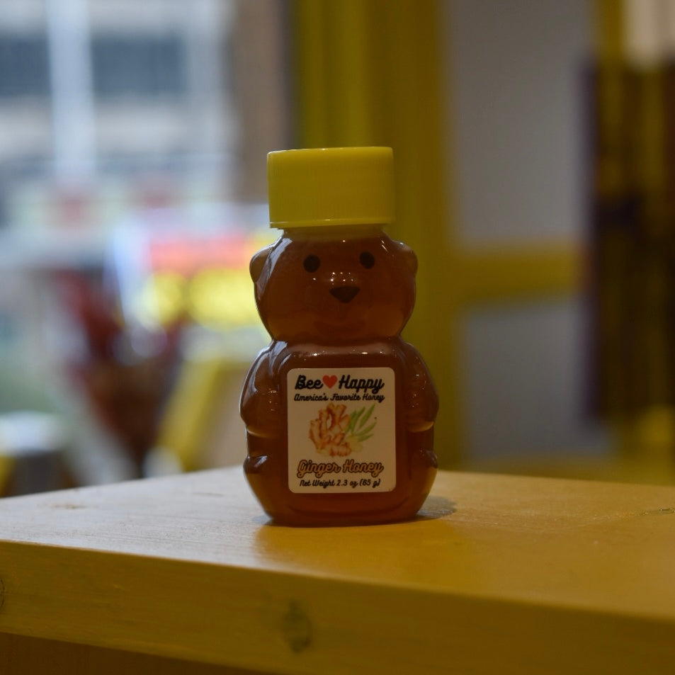 2.3 oz bear bottle of Ginger Honey on a wooden surface with a blurred background.
