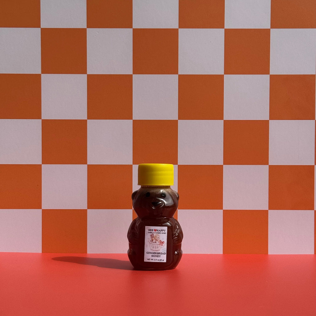 2.3 oz bear bottle of Bee Happy Gingerbread Honey against a checkered white and orange background.