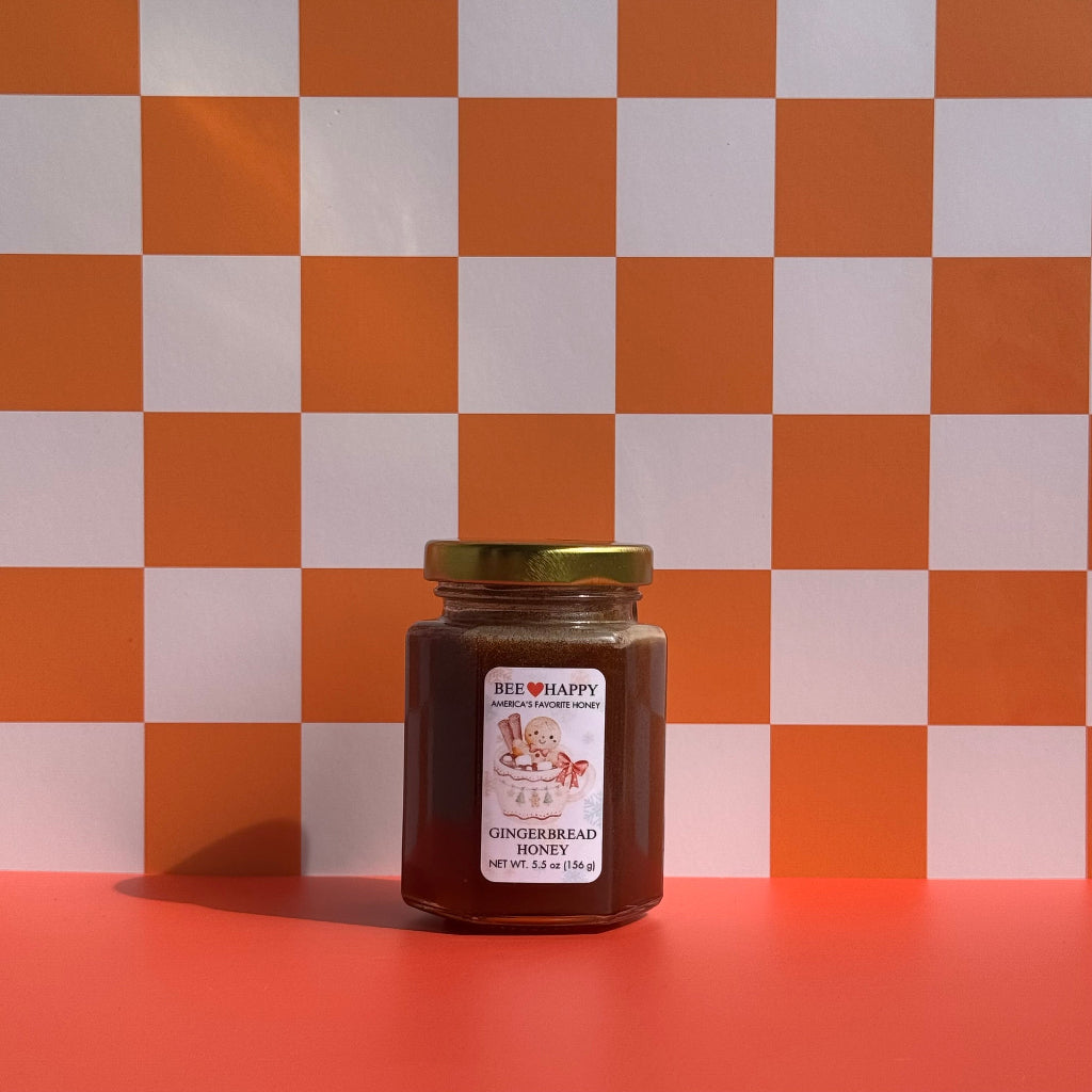 5.5 oz jar of Bee Happy Gingerbread Honey against a checkered white and orange background.