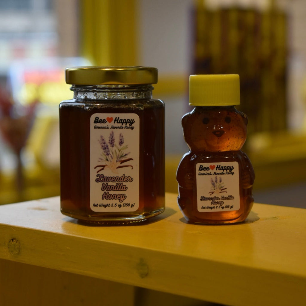 5.5 oz jar and 2.3 oz bear bottle of Lavender Vanilla Honey on a wooden surface with a blurred background.
