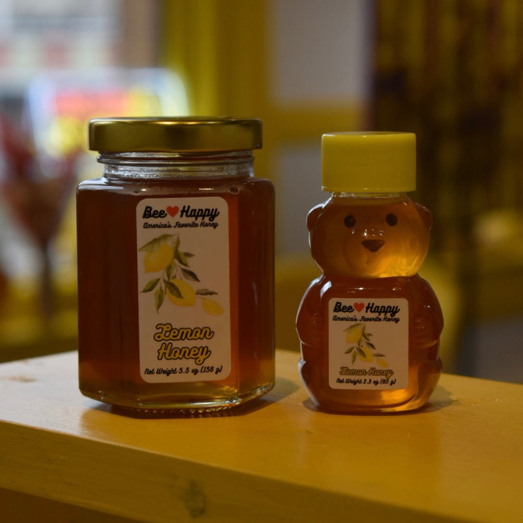 5.5 oz jar and 2.3 oz bear bottle of Lemon Honey on a wooden surface with a blurred background.