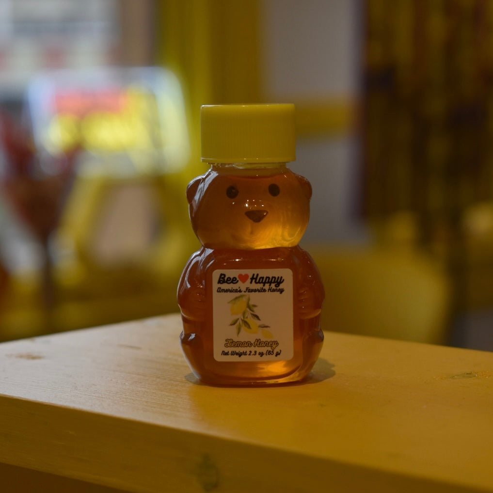 2.3 oz bear bottle of Lemon Honey on a wooden surface with a blurred background.