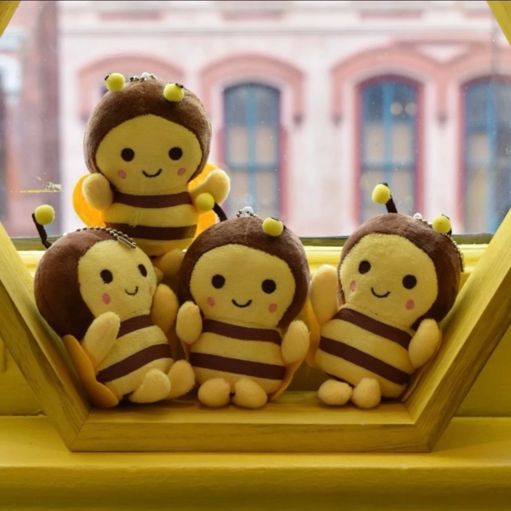 Four bee-shaped plush toys sitting on a yellow surface with a blurred building in the background.