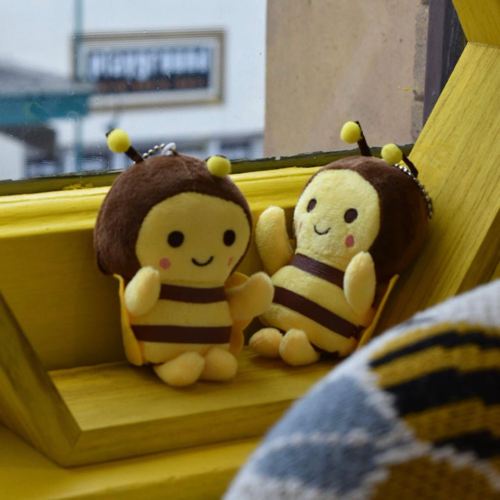 Two plush bee toys sitting on a wooden surface with a blurred background.
