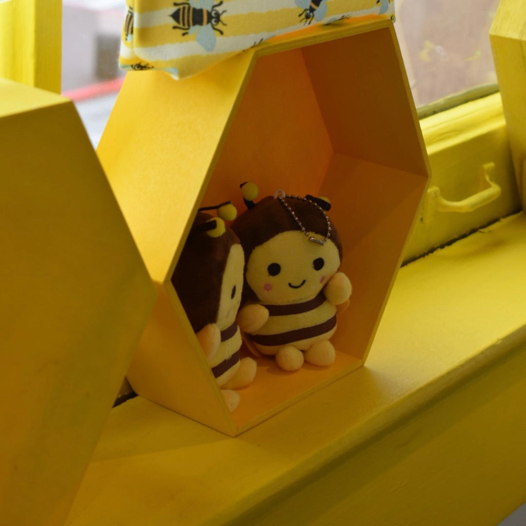Two bee-themed plush toys inside a yellow geometric shelf.