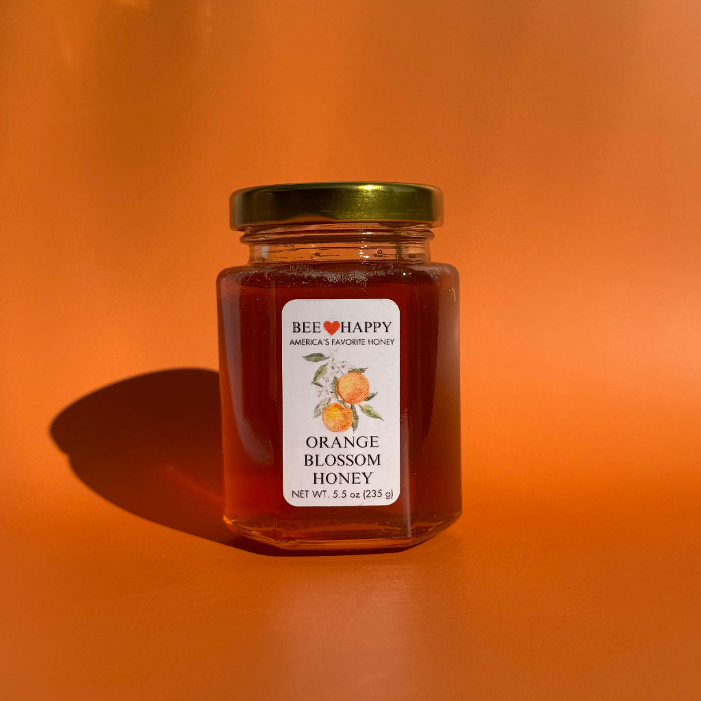 5.5 oz jar of Orange Blossom Honey against an orange background