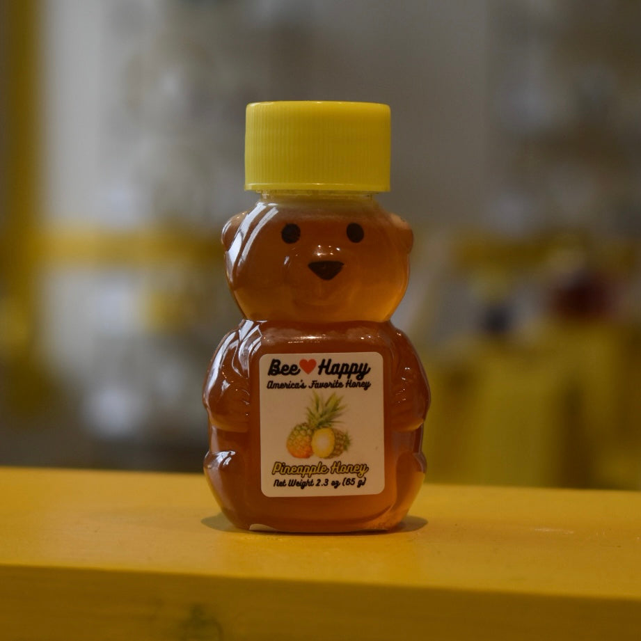 2.3 oz bear bottle of Pineapple Honey on a wooden surface with a blurred background.