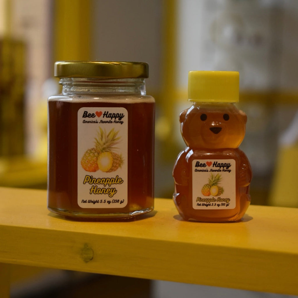 5.5 oz jar and 2.3 oz bear bottle of Pineapple Honey on a wooden surface with a blurred background.