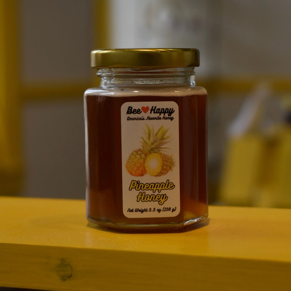 5.5 oz jar of Pineapple Honey on a wooden surface with a blurred background.