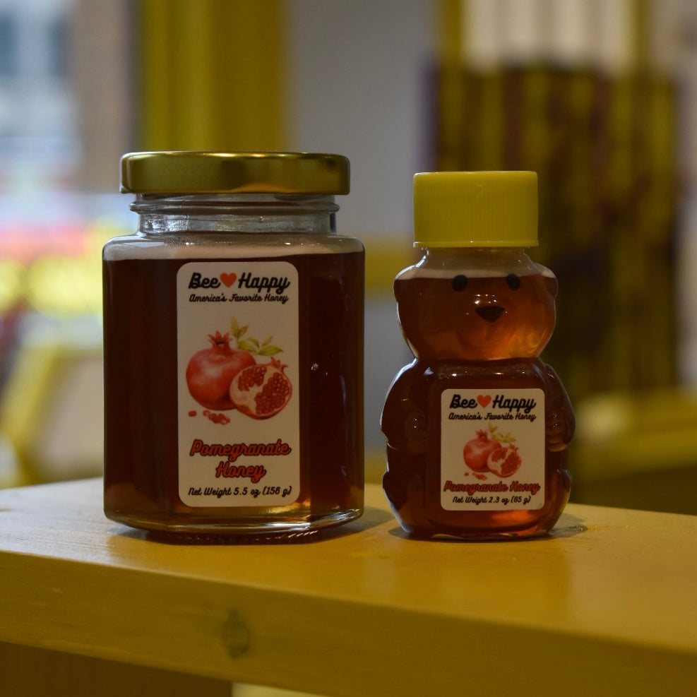 5.5 oz jar and 2.3 oz bear bottle of Pomegranate Honey on a wooden surface with a blurred background.