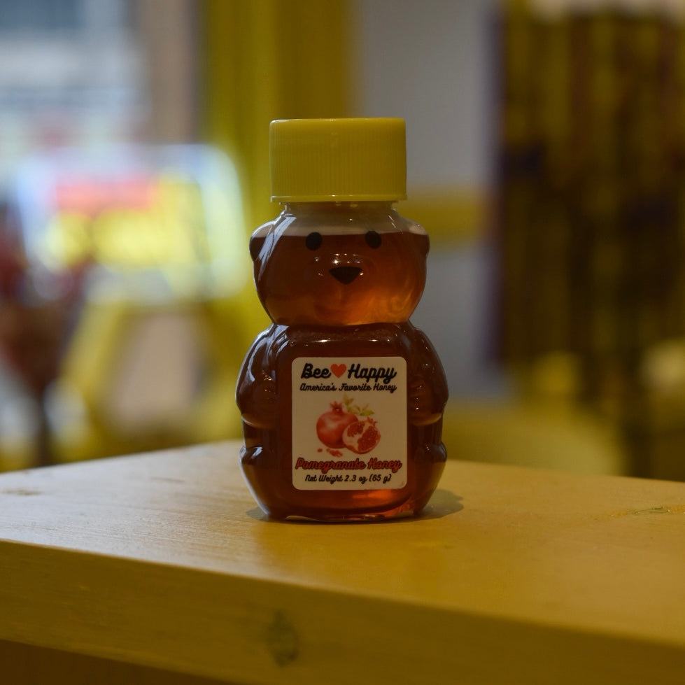 2.3 oz bear bottle of Pomegranate Honey on a wooden surface with a blurred background.