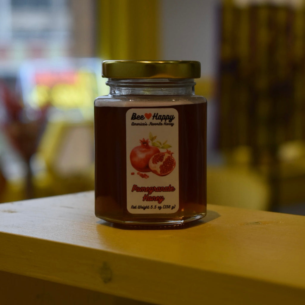 5.5 oz jar of Pomegranate Honey on a wooden surface with a blurred background.