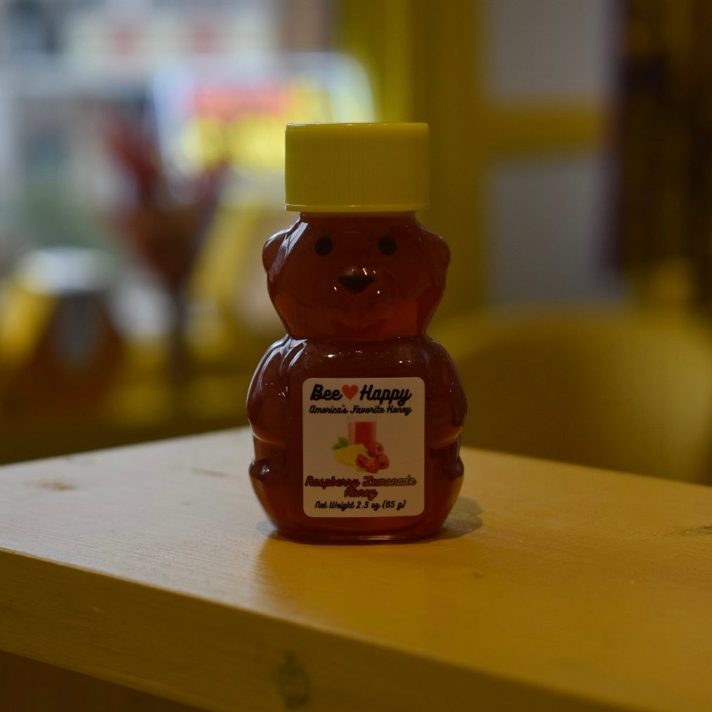 2.3 oz bear bottle of Raspberry Lemonade Honey on a wooden surface with a blurred background.