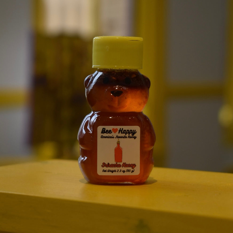 2.3 oz bear bottle of Sriracha Honey on a wooden surface with a blurred background.