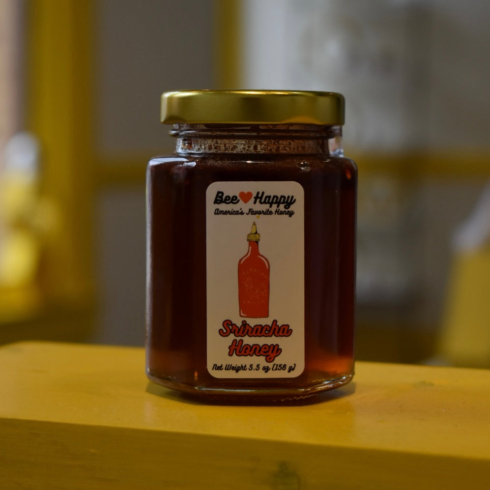 5.5 oz jar of Sriracha Honey on a wooden surface with a blurred background.
