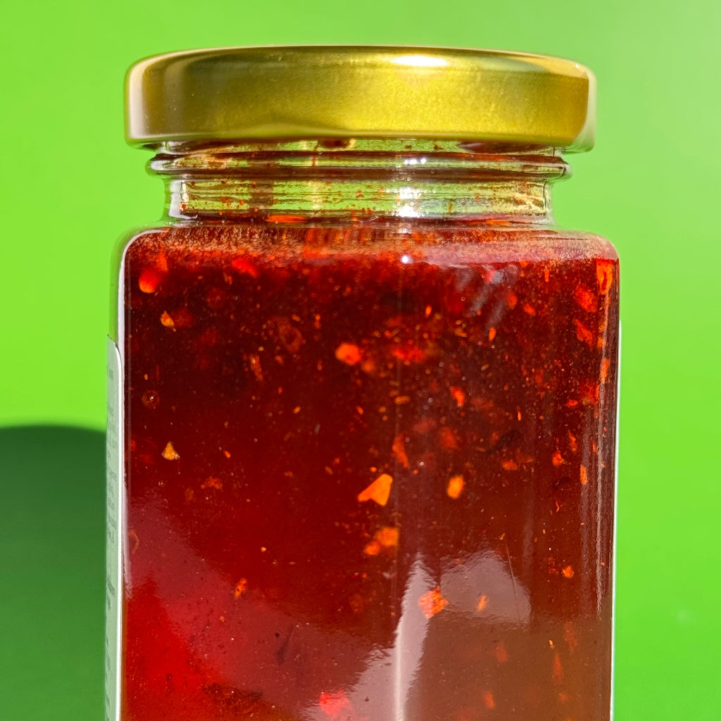 Sideways closeup of 5.5 oz jar of Sriracha Honey with a green background