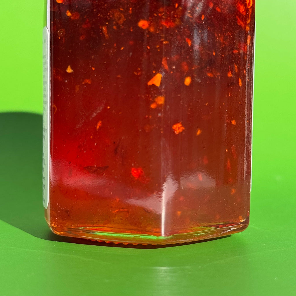 Sideways closeup of 5.5 oz jar of Sriracha Honey with a green background