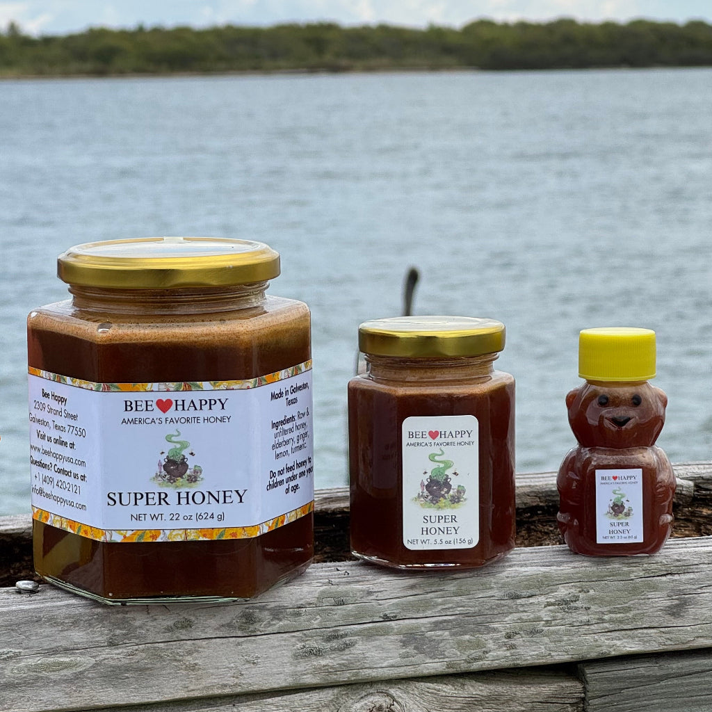 22 oz jar, 5.5 oz jar and 2.3 oz bear bottle of Super Honey on a wooden surface with the sea in the background
