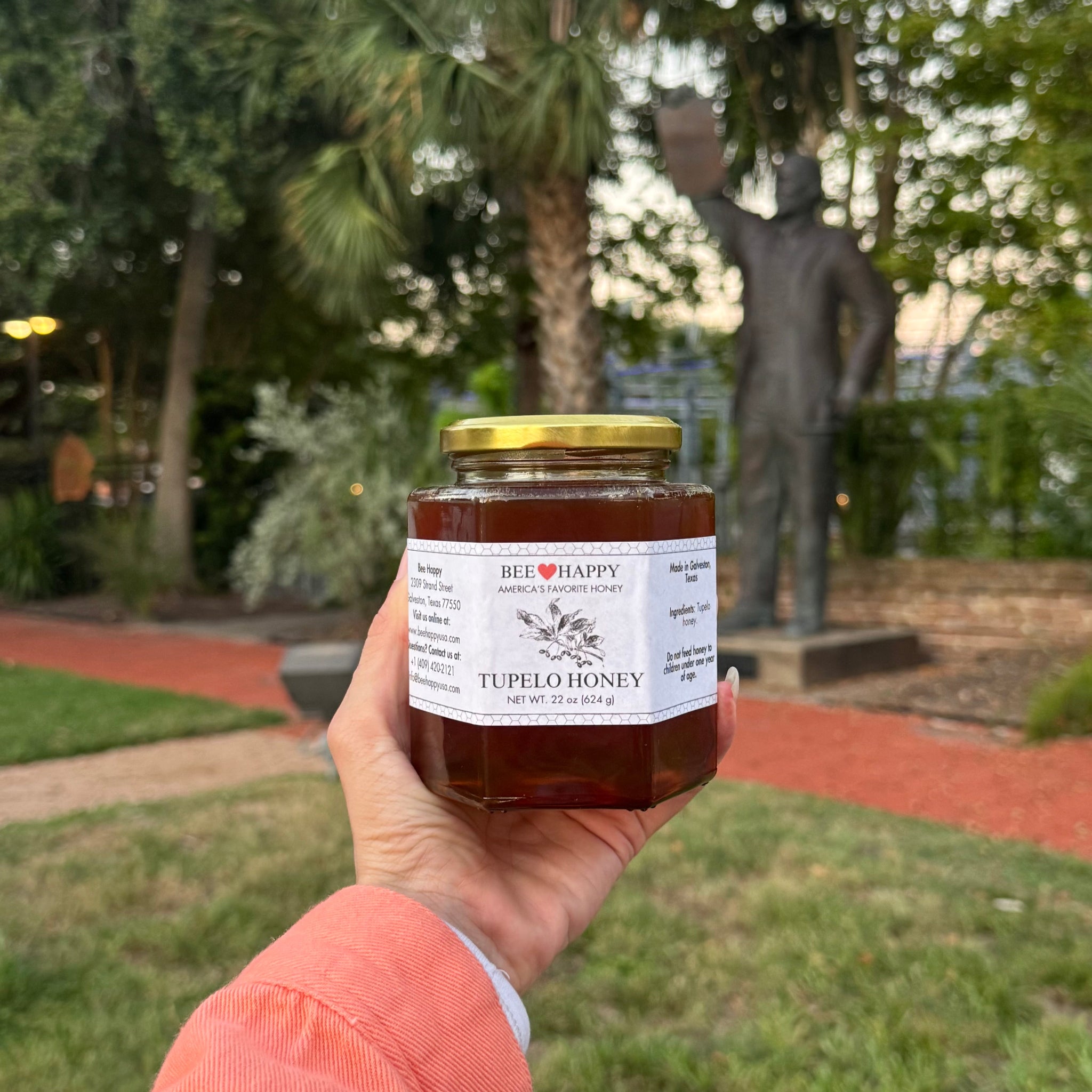 22 oz Jar of Tupelo Honey held in a hand with a park background
