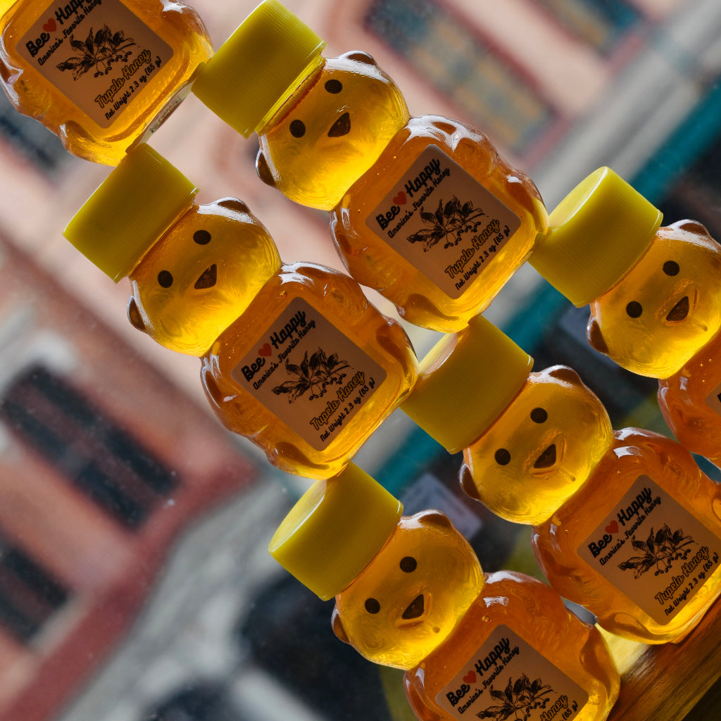 2.3 oz bear bottles of Tupelo Honey against a window background standing on top of each other in a triangle formation