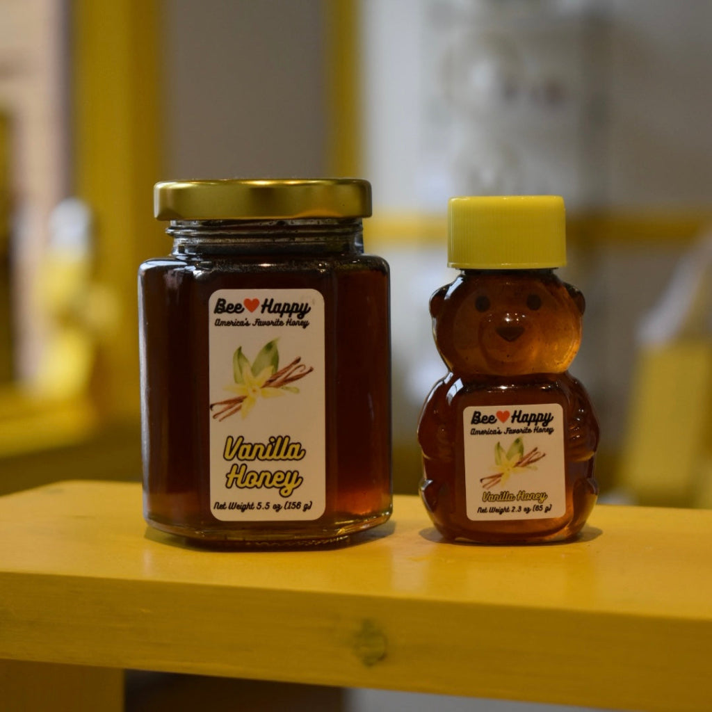 5.5 oz jar and 2.3 oz bear bottle of Vanilla Honey on a wooden surface with a blurred background.