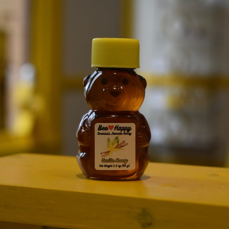 2.3 oz bear bottle of Vanilla Honey on a wooden surface with a blurred background.