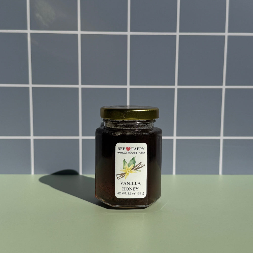5.5 oz jar of Bee Happy Vanilla Honey on a gray checkered background