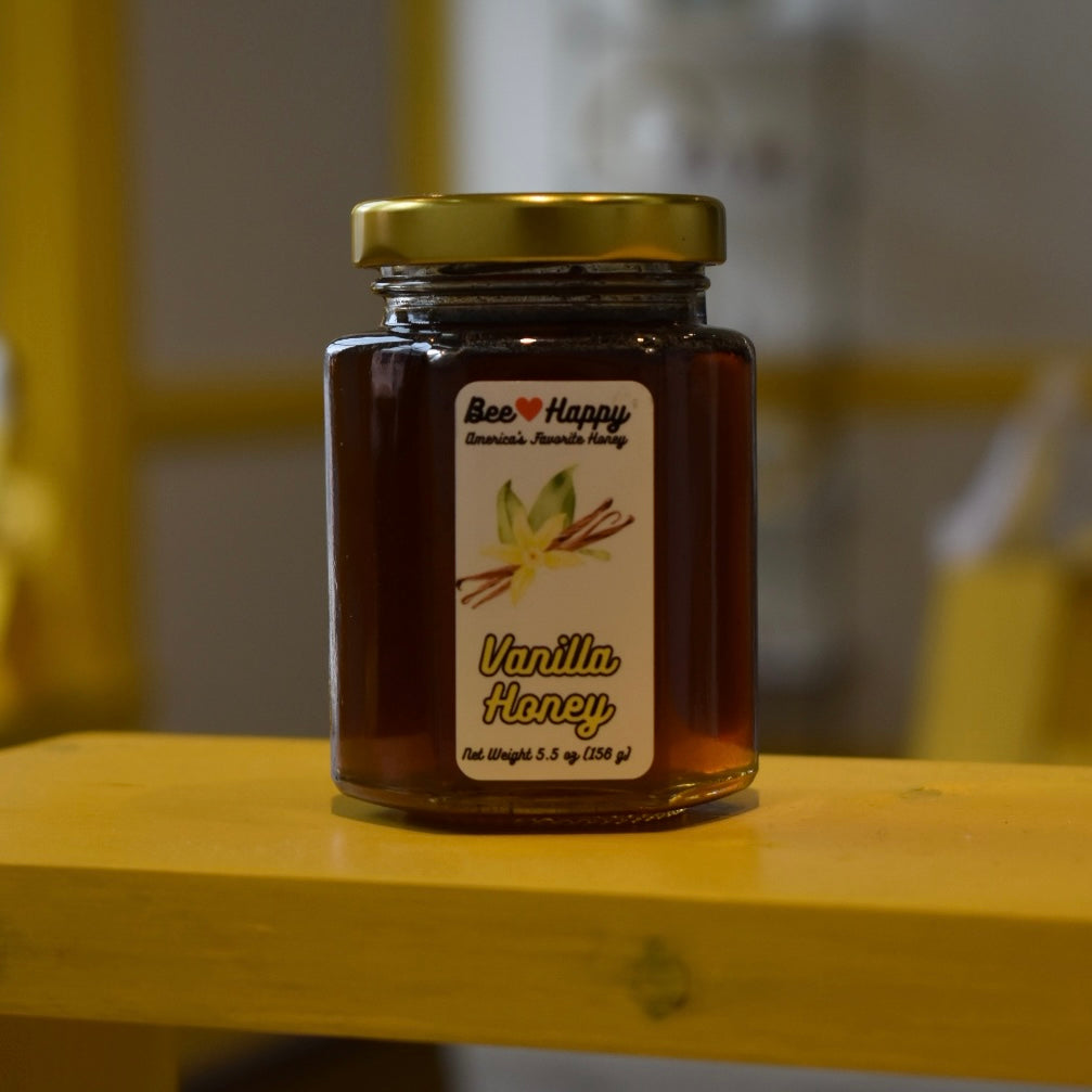 5.5 oz jar of Vanilla Honey on a wooden surface with a blurred background.
