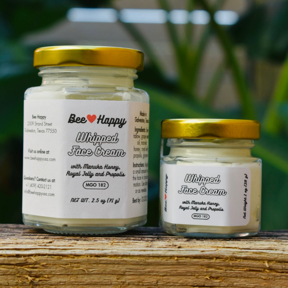 1 oz jar and 2.5 oz jar of Whipped Face Cream on a wooden surface with a blurry green background