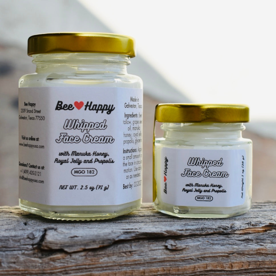 1 oz jar and 2.5 oz jar of Whipped Face Cream on a wooden surface with a blurry beige background
