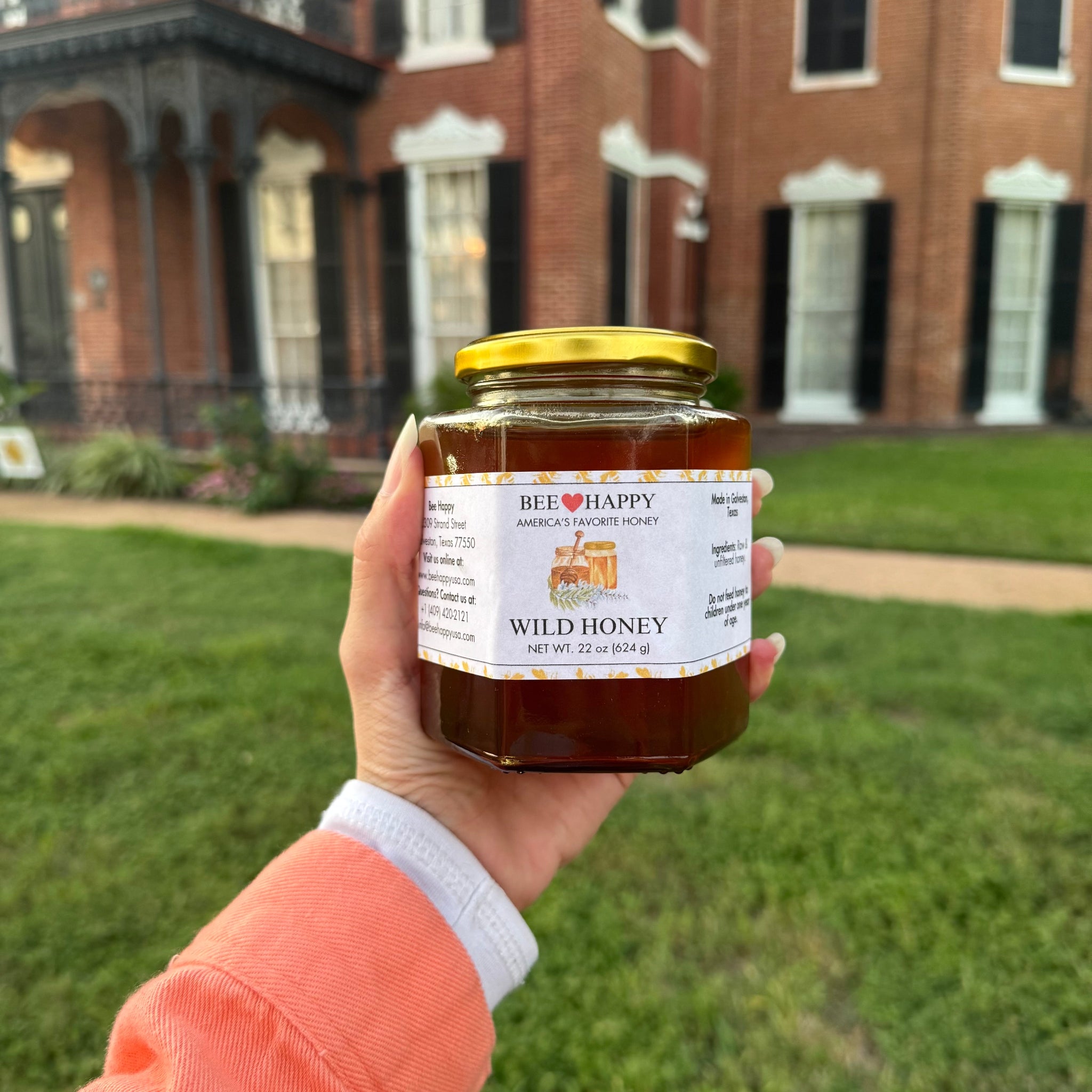 22 oz Jar of Wild Honey held in a hand with an old house in the backgroud